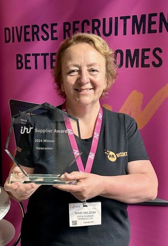 A woman is holding a trophy in front of a sign that says `` diverse recruitmen better homes ''.