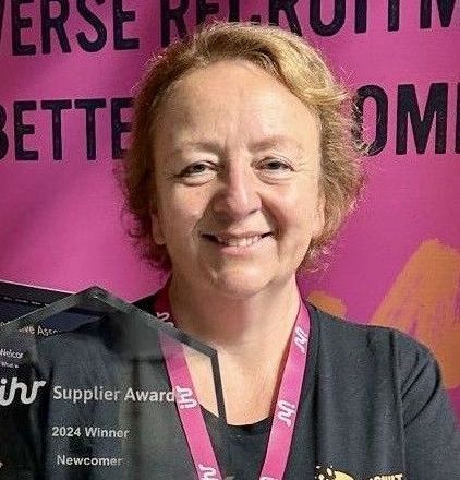 A woman is holding a trophy in front of a pink background.