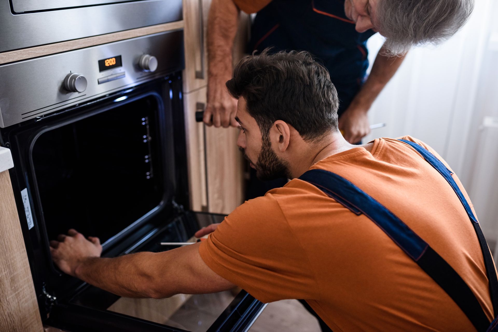 Two people loading a hot pan into a built-in oven in a kitchen