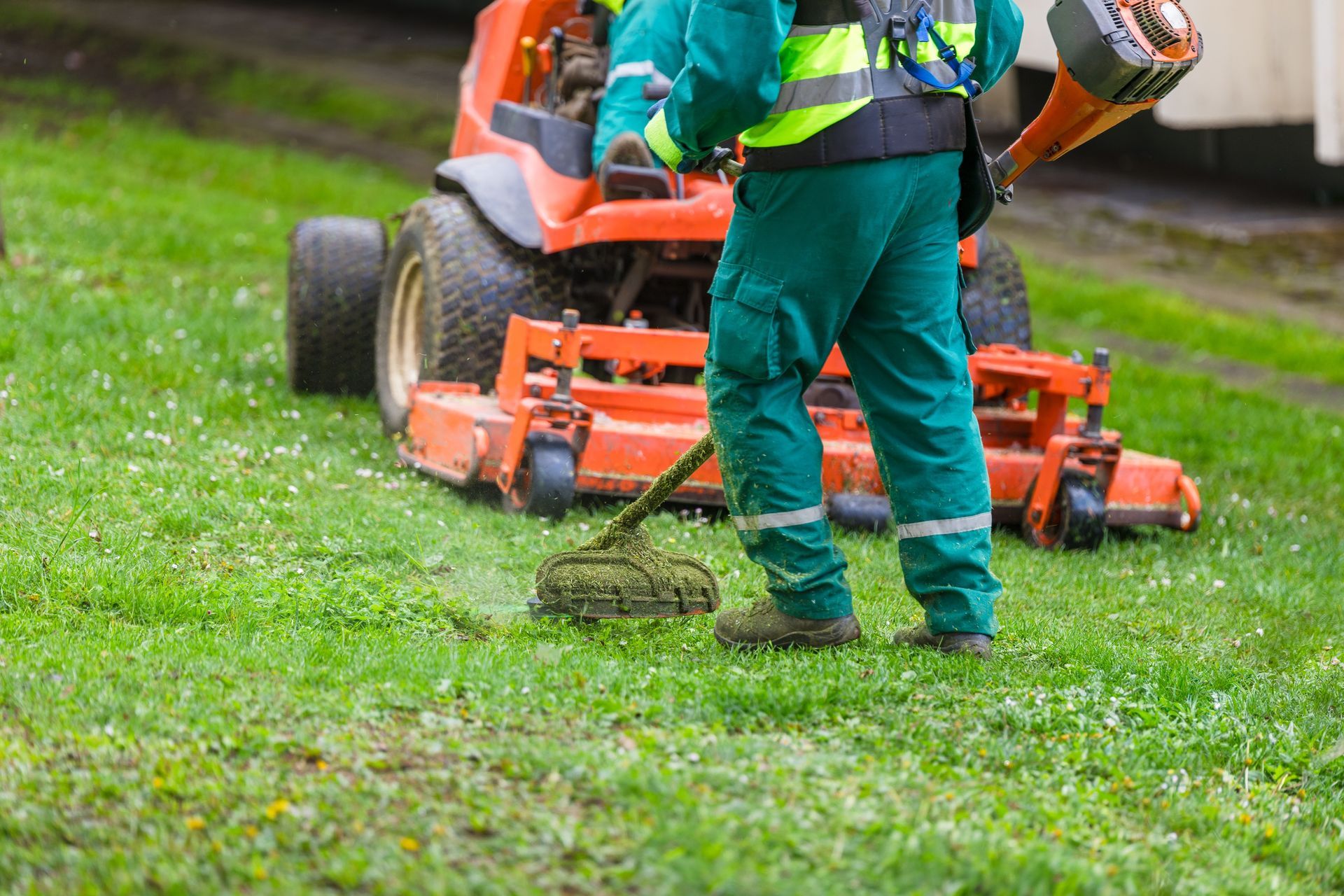 Person in green workwear mowing a lawn with an orange ride-on mower