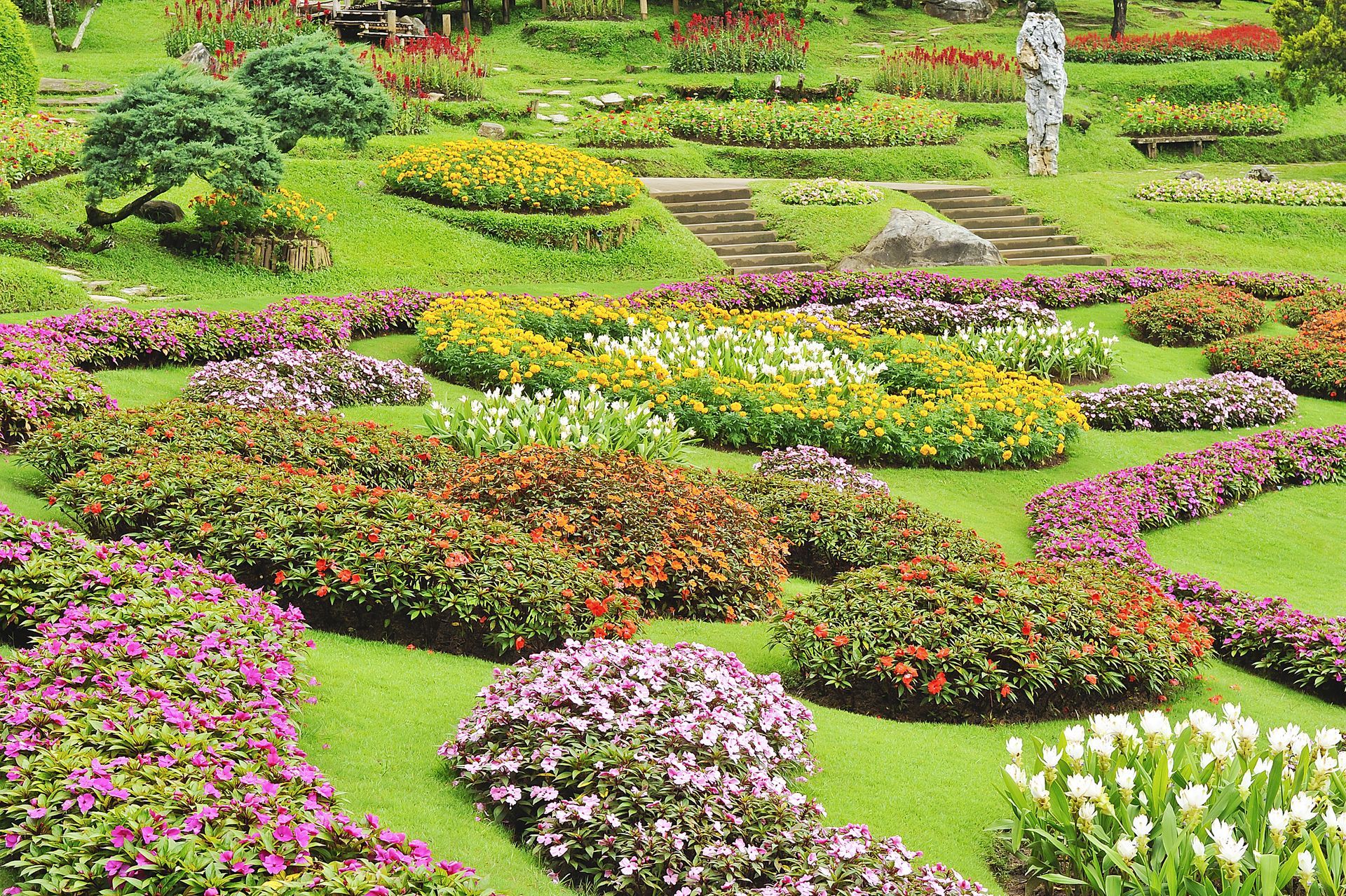 Colorful flower beds arranged in a landscaped garden with winding paths and a statue in the background