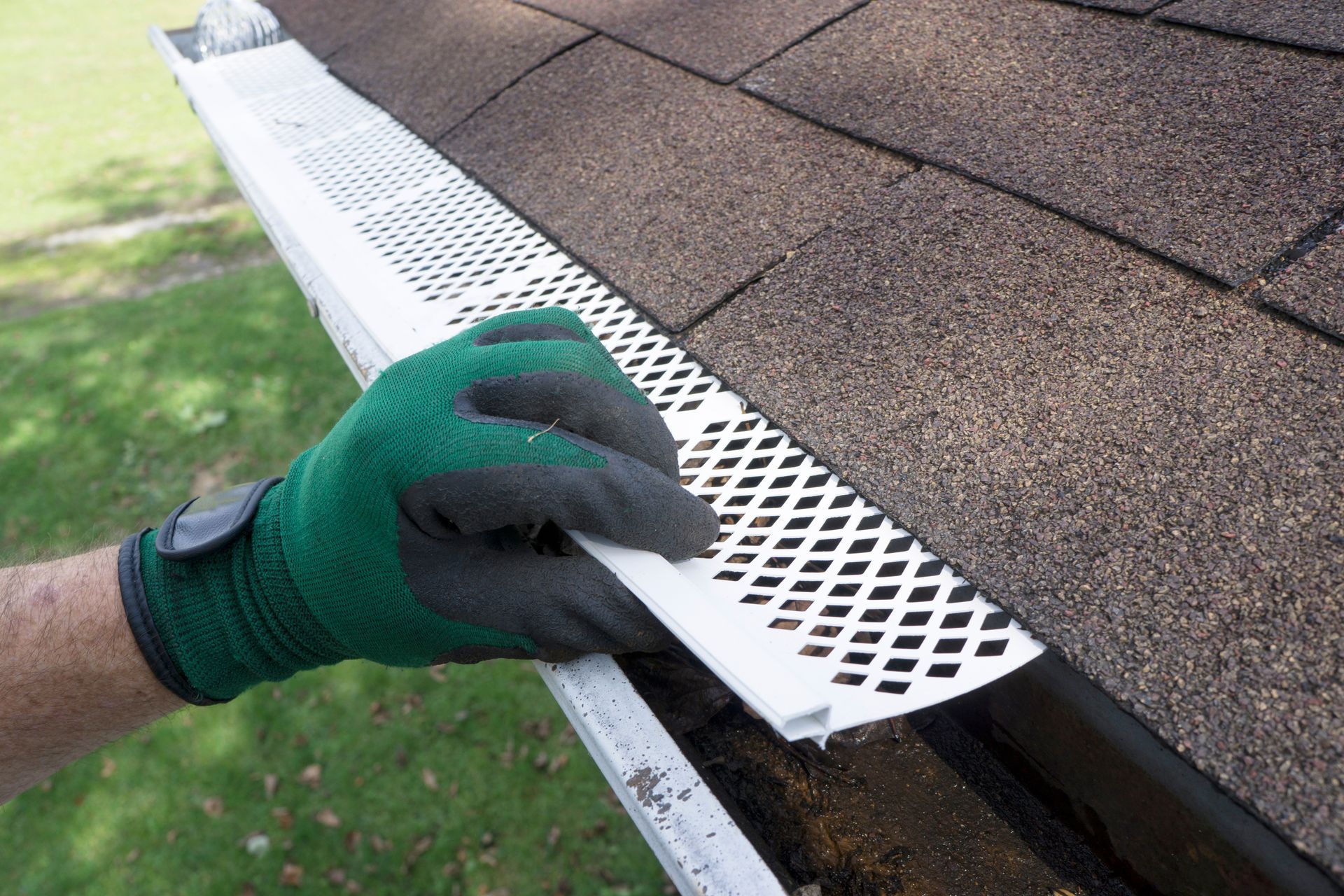 A person wearing gloves is cleaning a gutter on a roof.