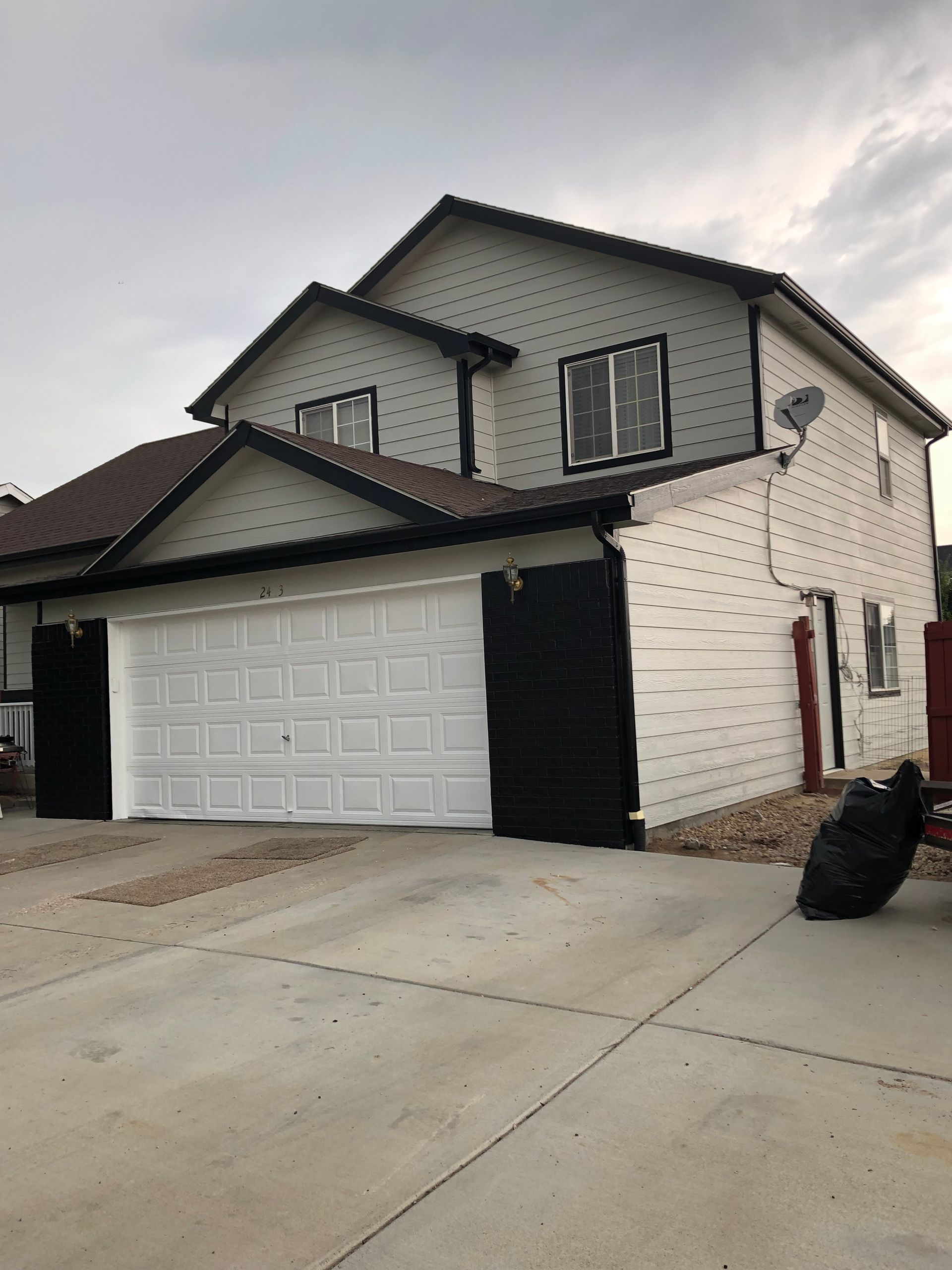 A White House With A Black Garage Door And A Satellite Dish On The Roof