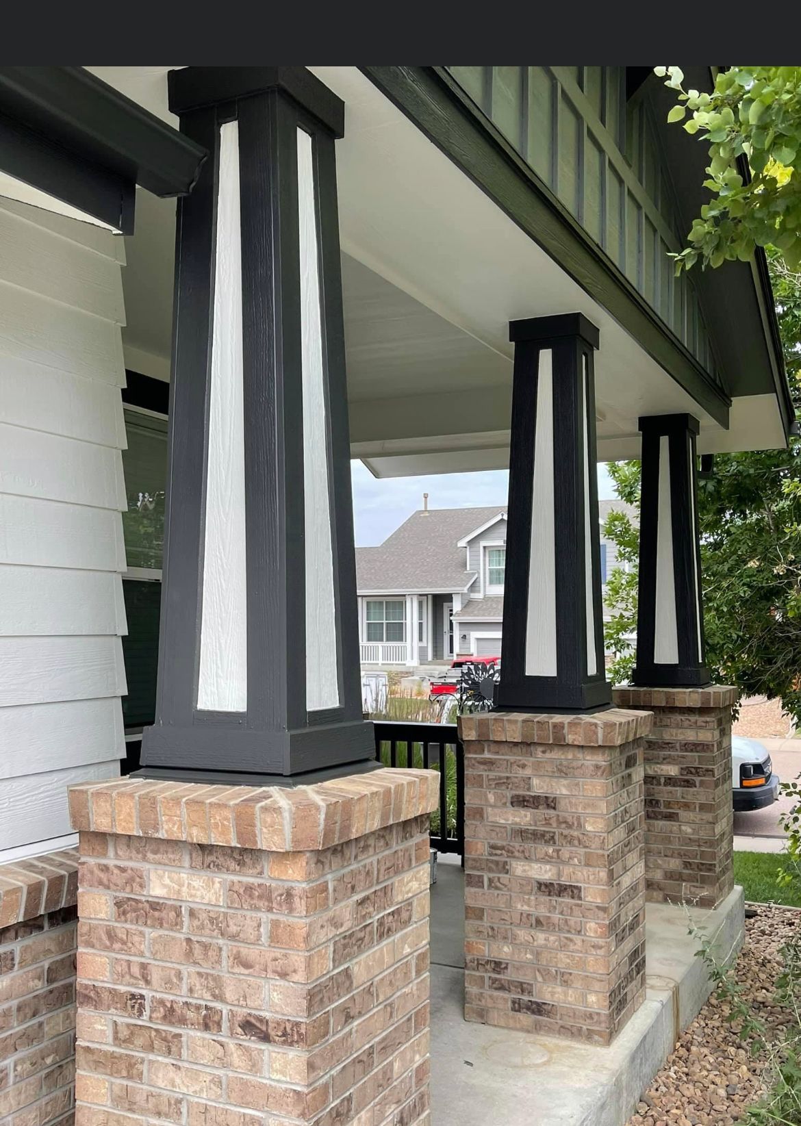 A Brick Porch With Black And White Columns And A White House In The Background