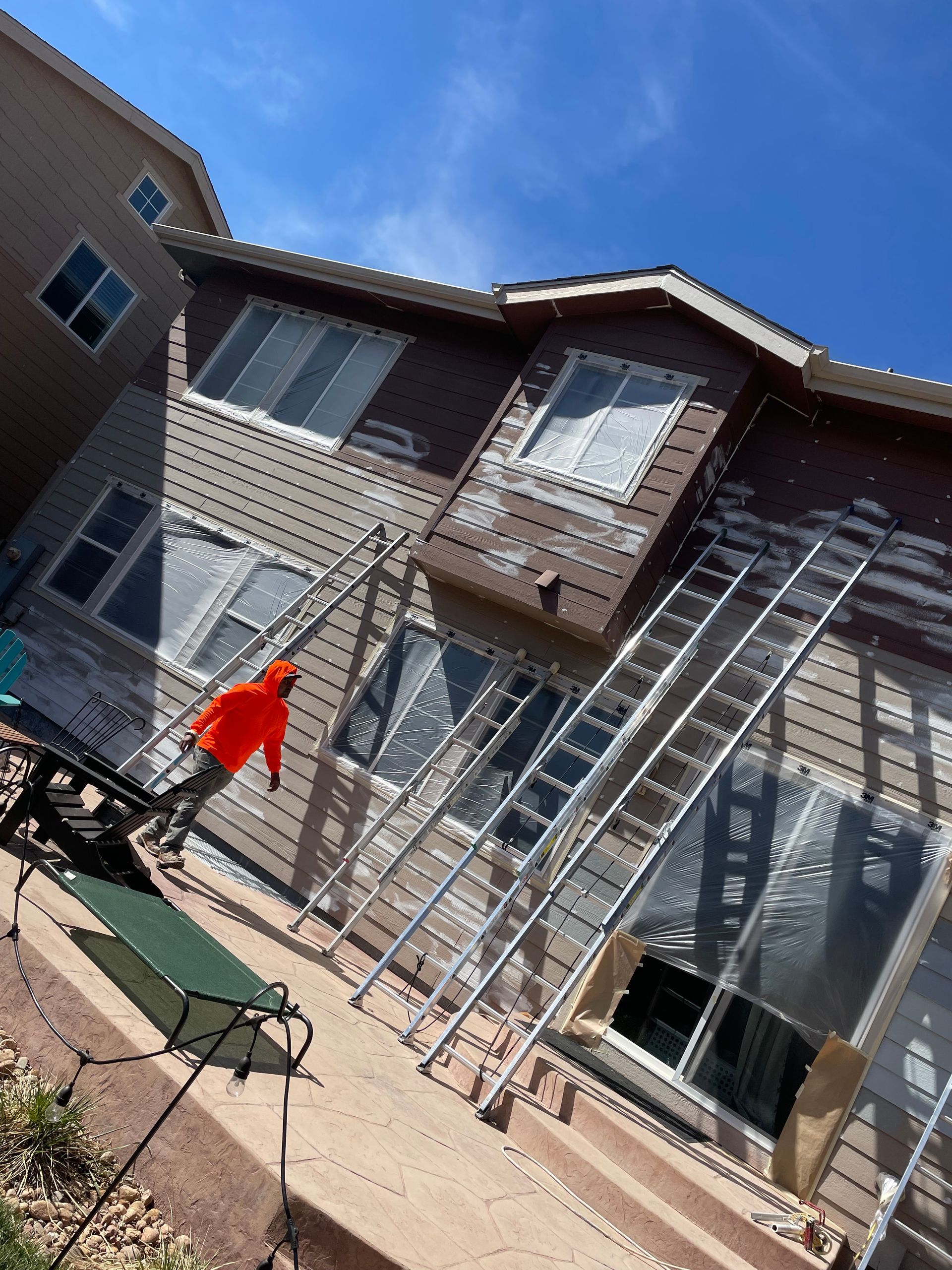 A Man In An Orange Jacket Is Standing On A Ladder In Front Of A House