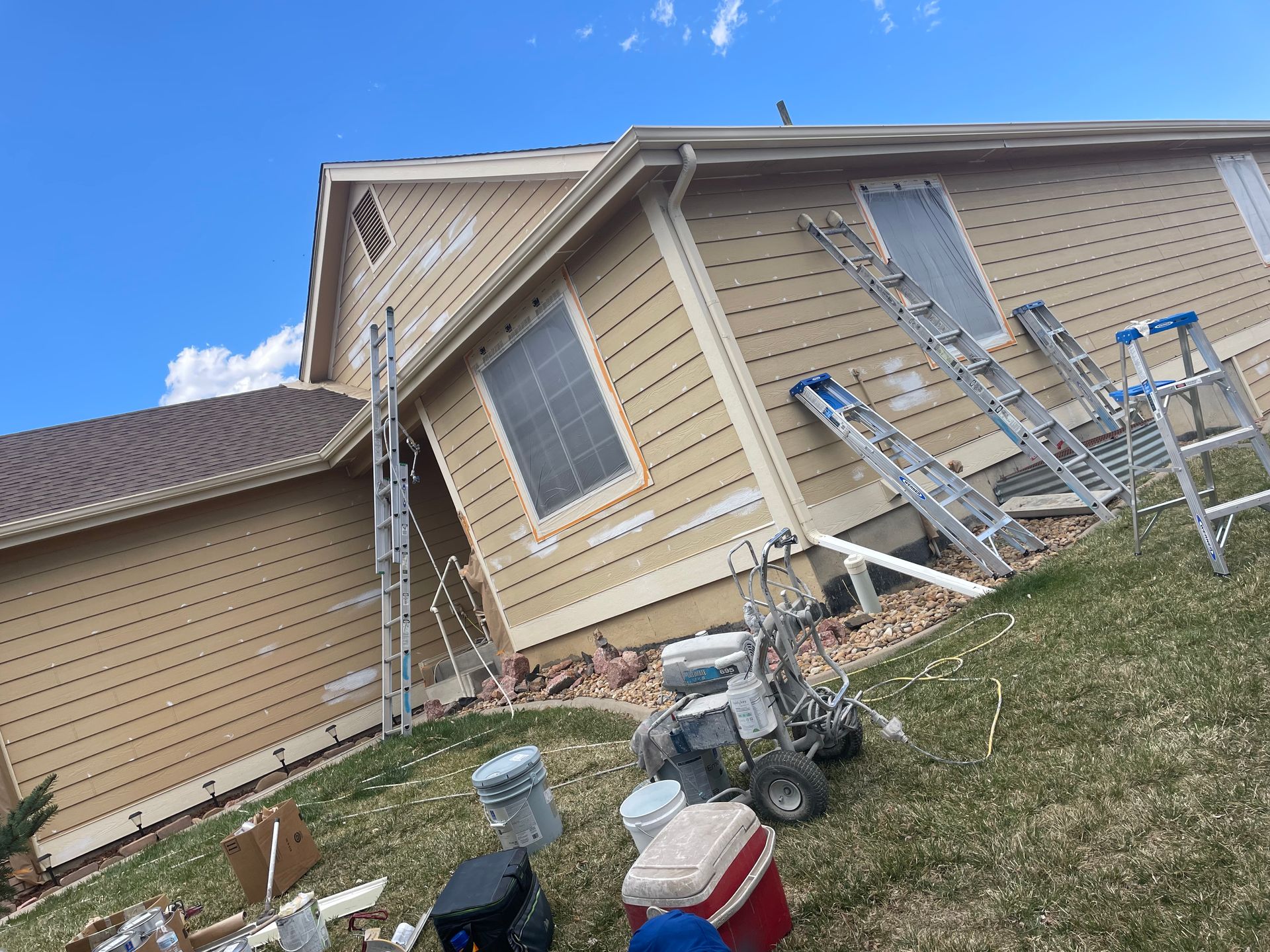 A House Is Being Painted In A Yard With Buckets And Ladders