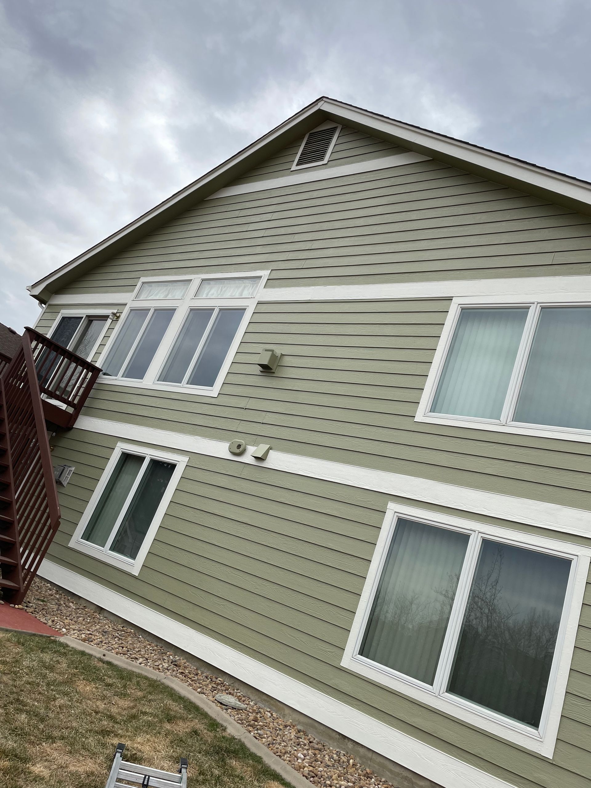 A Large Green House With A Lot Of Windows And Stairs