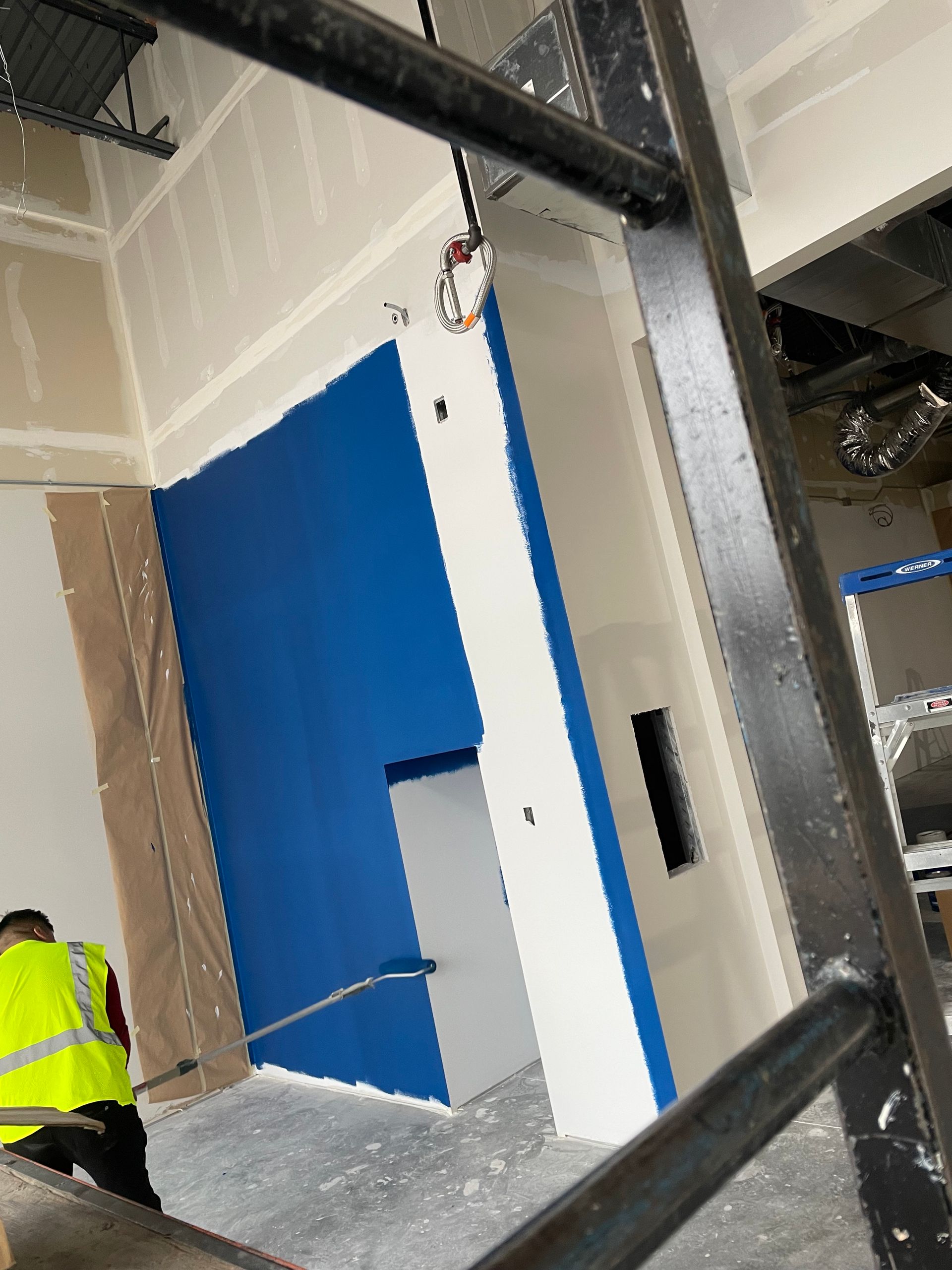 A Man In A Yellow Vest Is Standing In A Room With Blue Walls