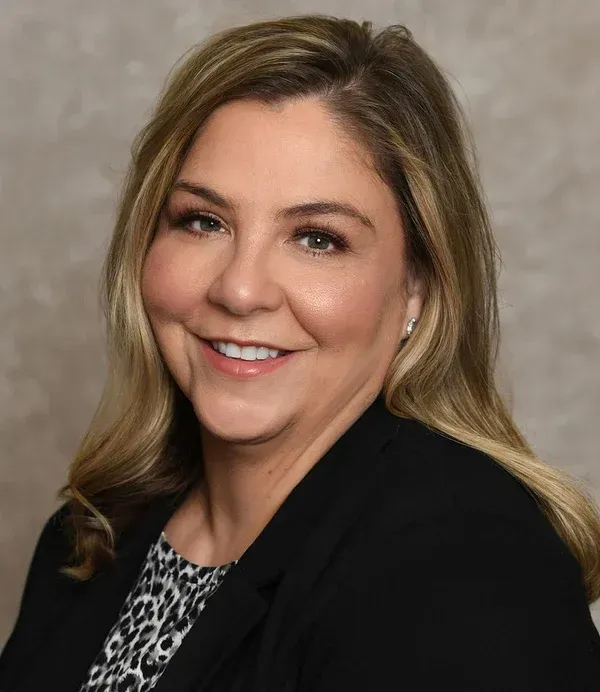 A woman wearing a black jacket and a leopard print shirt is smiling for the camera.