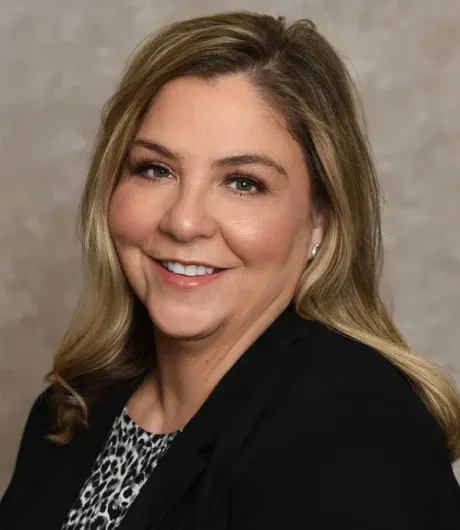 A woman wearing a black jacket and a leopard print shirt is smiling for the camera.