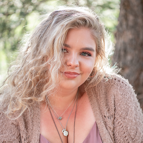 A woman wearing a sweater and a necklace is sitting in front of a tree.