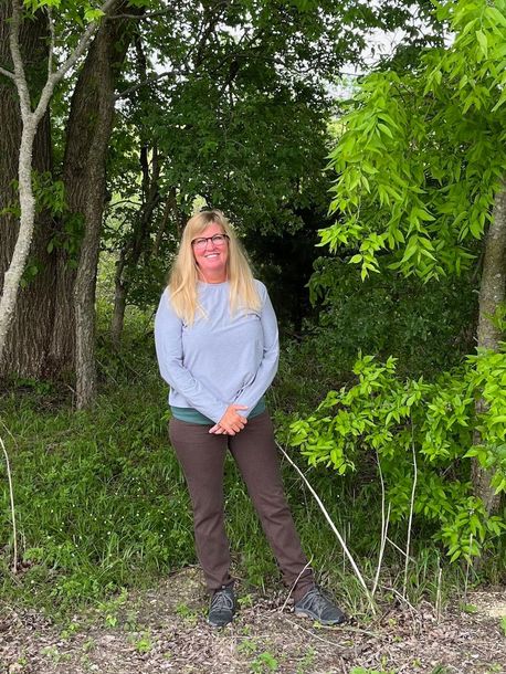 A woman wearing a sweater and a necklace is sitting in front of a tree.
