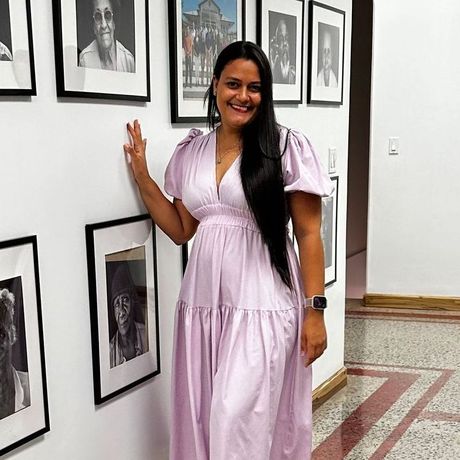 A woman in a purple dress is leaning against a wall with pictures on it