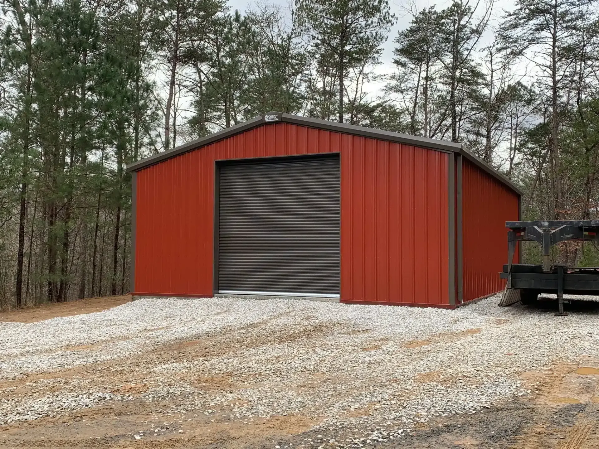 a red metal garage with a black door is sitting on top of a gravel lot .