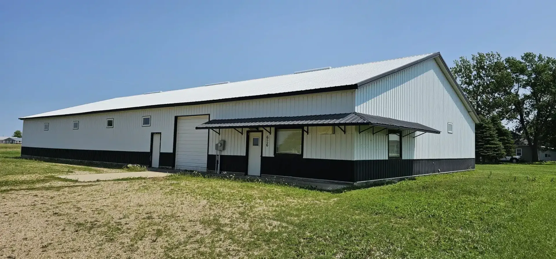 a white and black barn is sitting in the middle of a grassy field .
