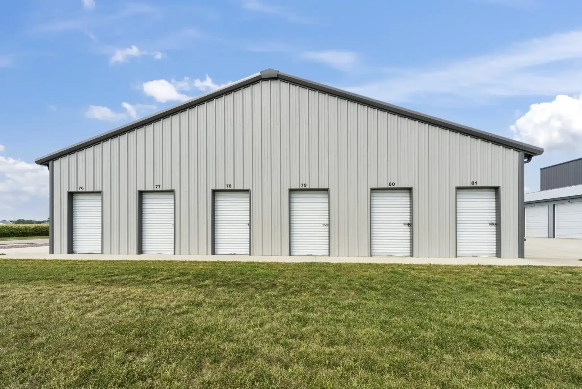 a large metal building with a lot of doors is sitting on top of a lush green field .