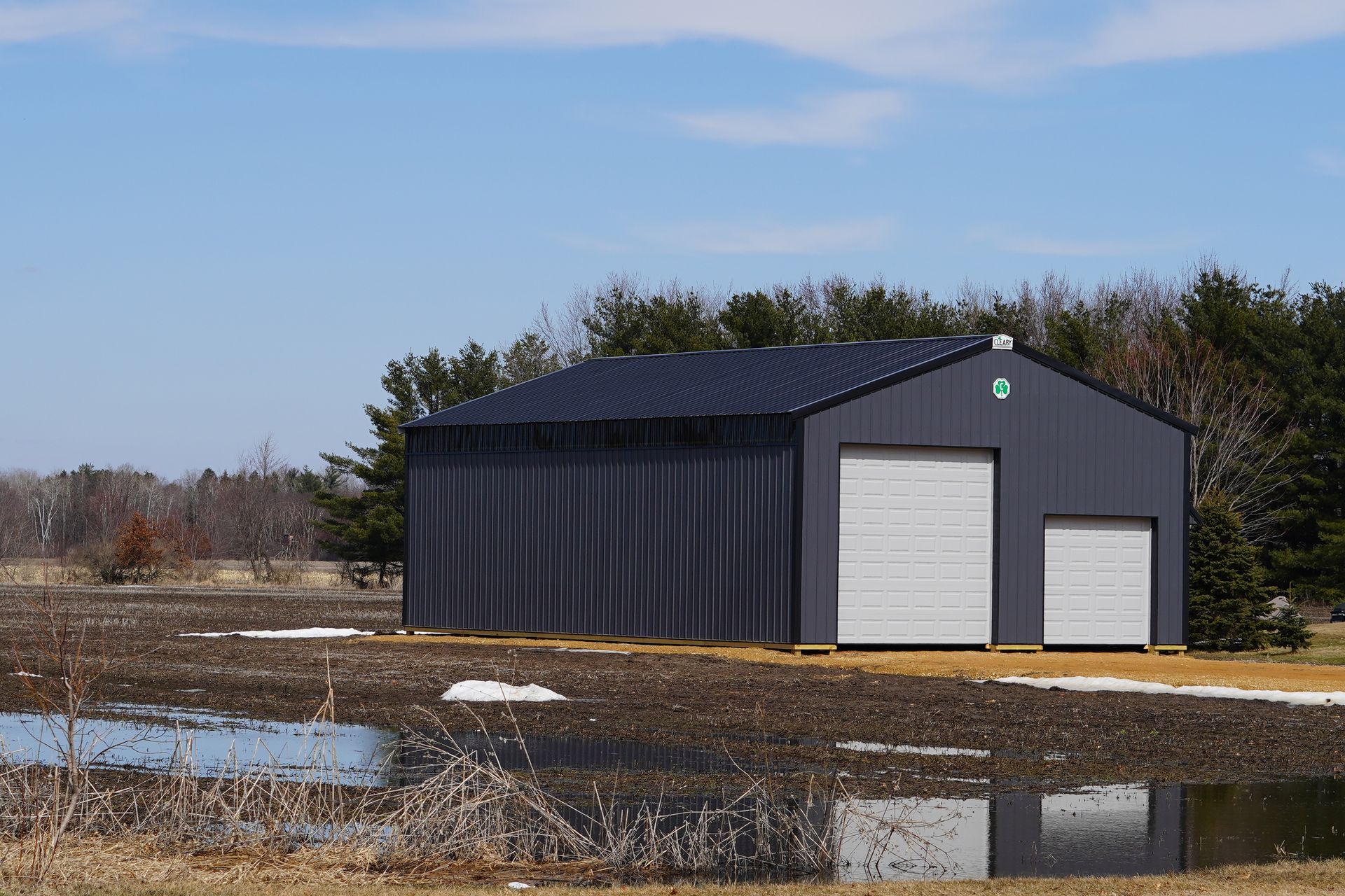 a black building with white doors is in the middle of a muddy field