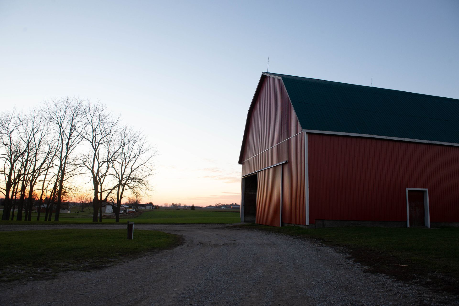 a red barn with a green roof is in the middle of a dirt road