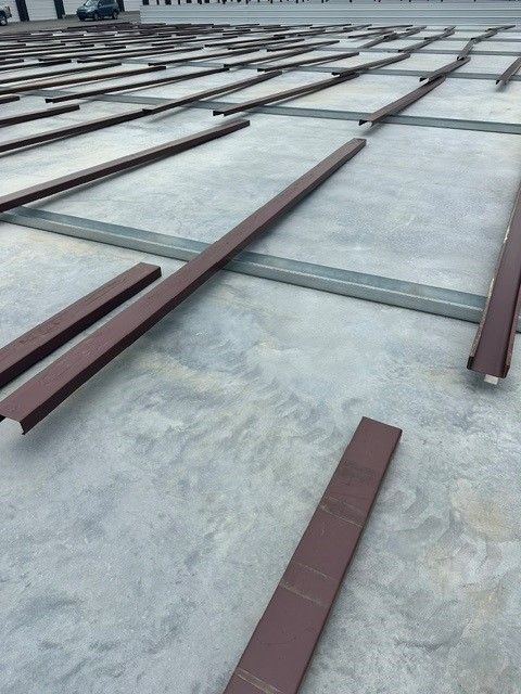 Rows of brown metal beams laid across a concrete rooftop or terrace under construction.