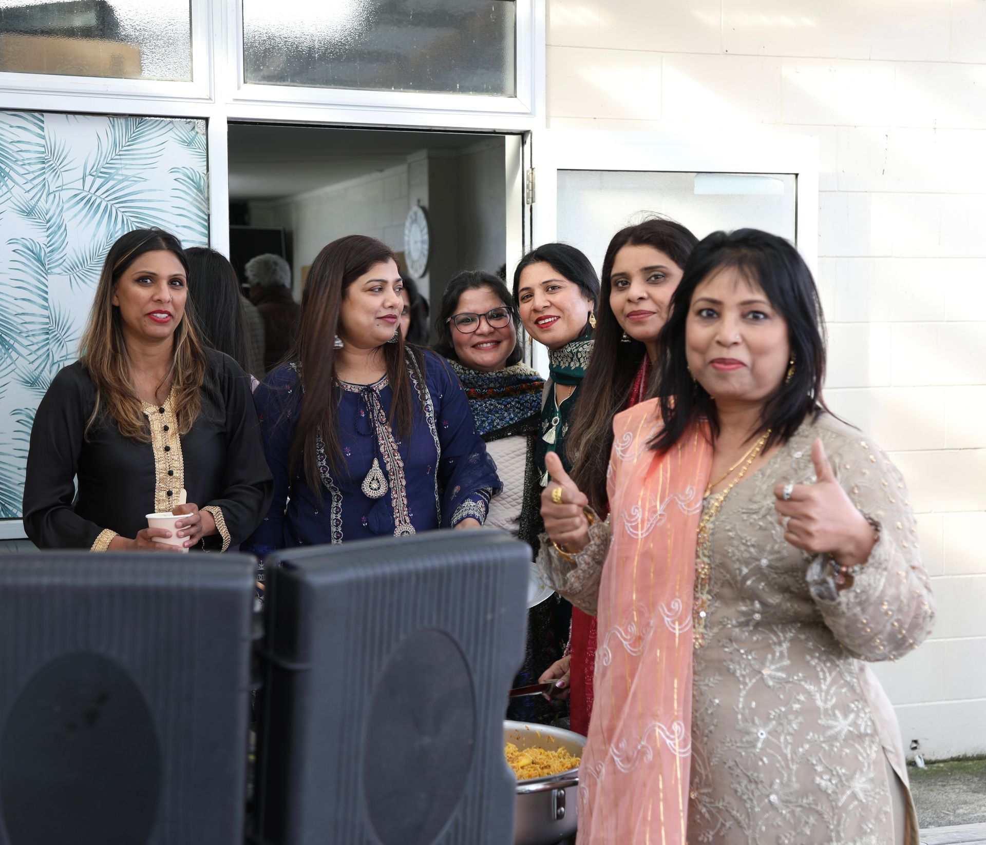 Man in suit speaking at podium, gesturing. Green-lit stage with Christmas tree and background text visible.