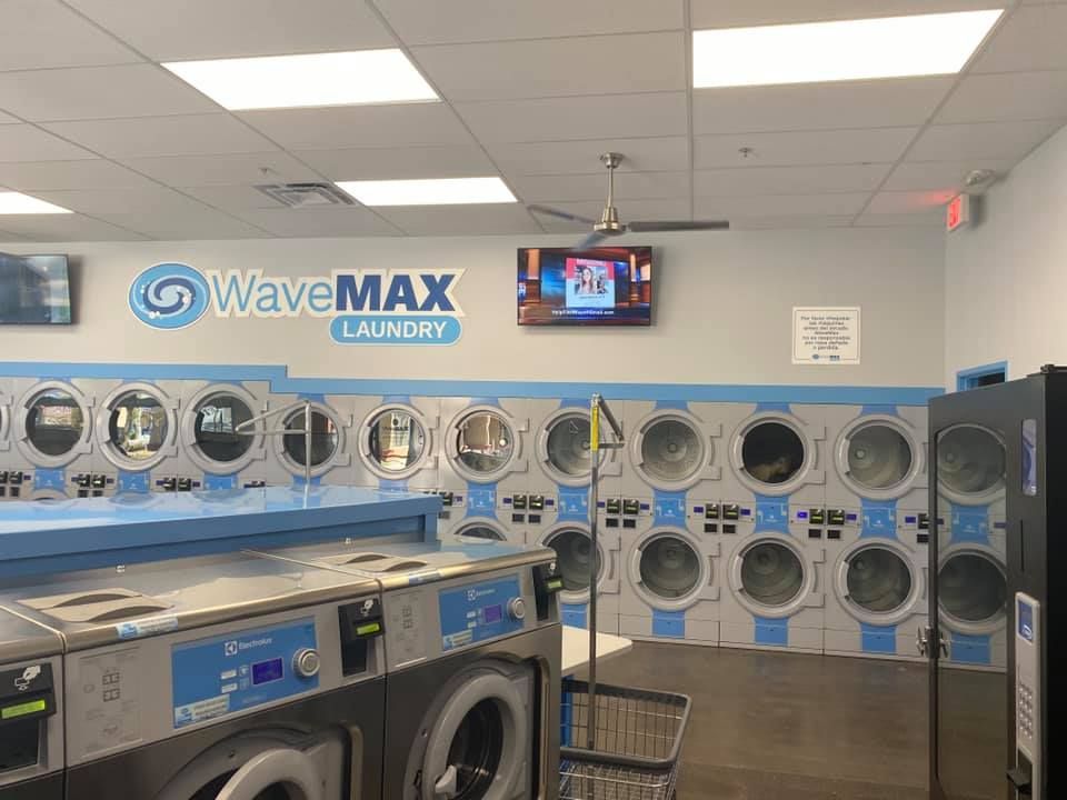 A bright, clean WaveMAX Laundry facility with rows of blue and white washers and dryers under recessed ceiling lights.