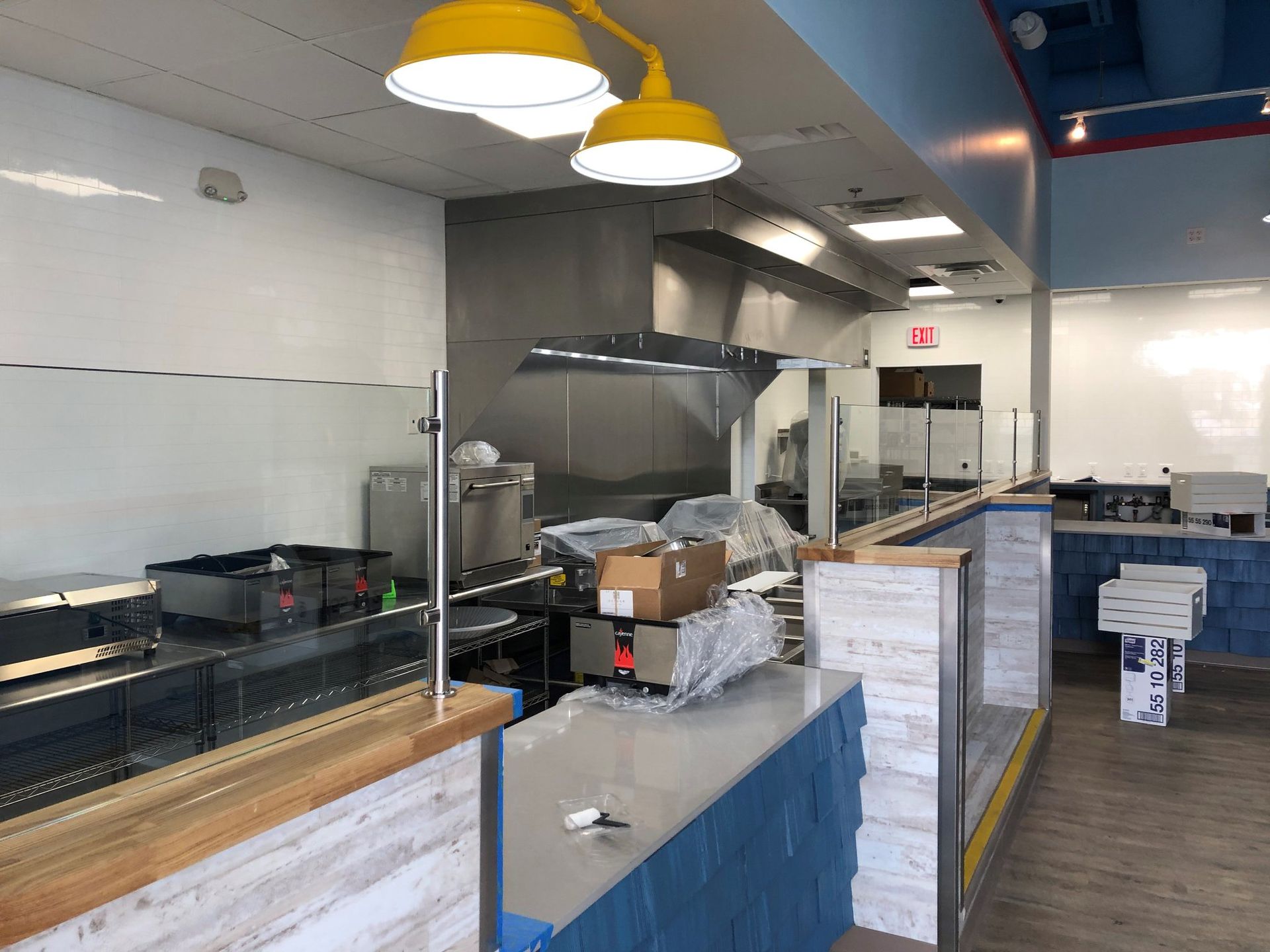 An interior view of a commercial kitchen counter with light wood accents, blue cabinets, and two yellow pendant lights.