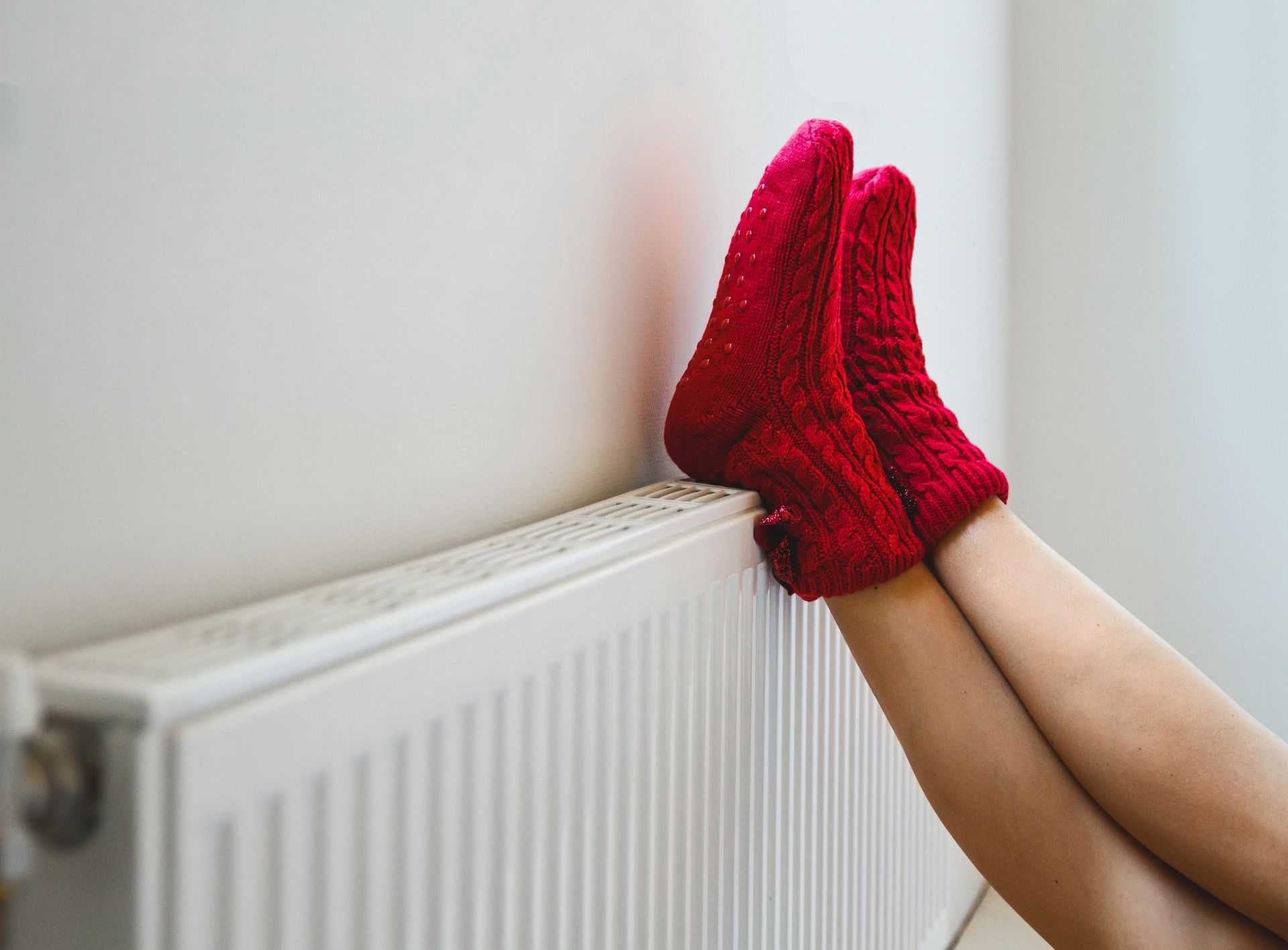 A person wearing red socks is warming their feet on a radiator.