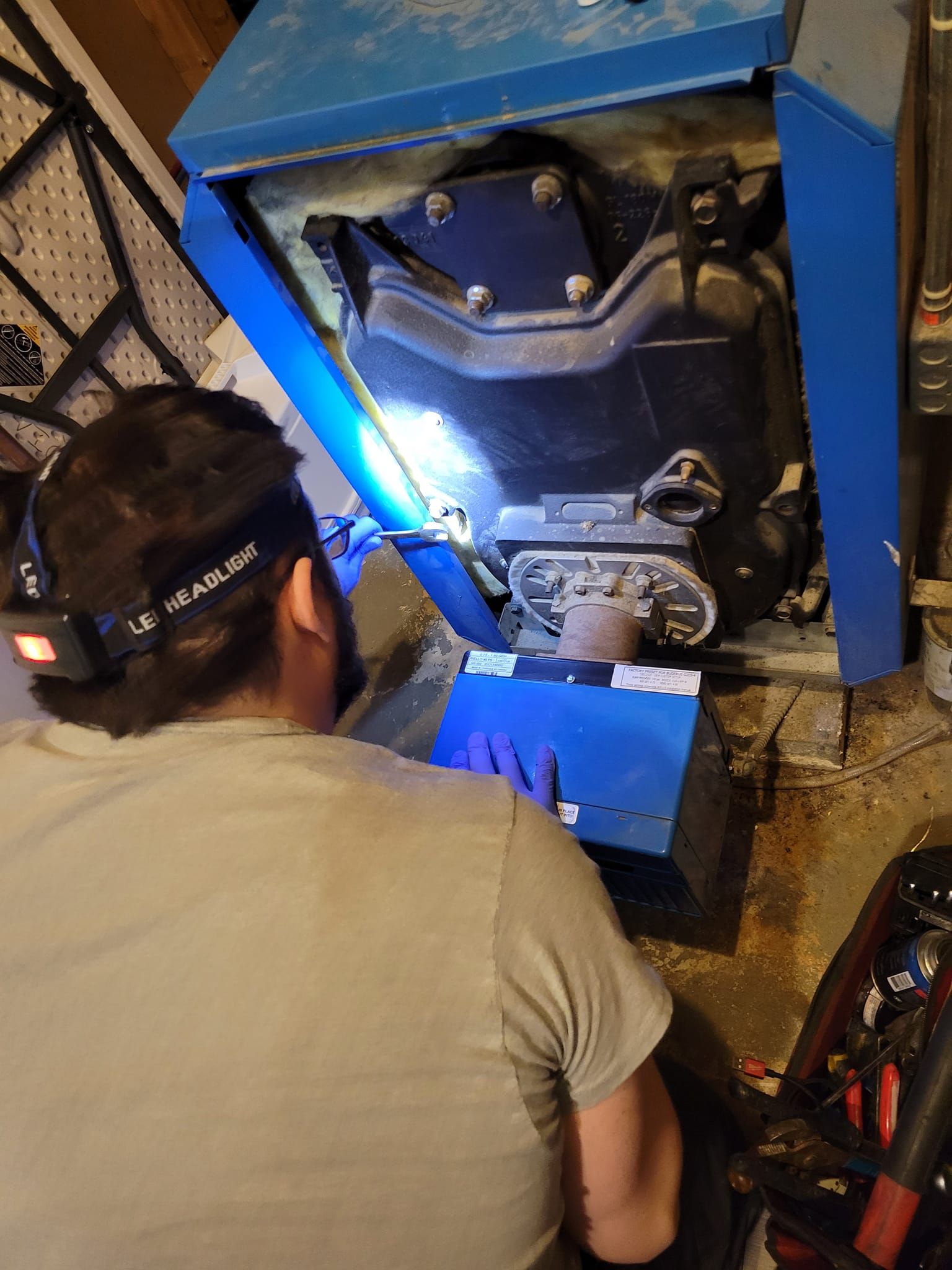A man is working on a blue boiler in a basement.