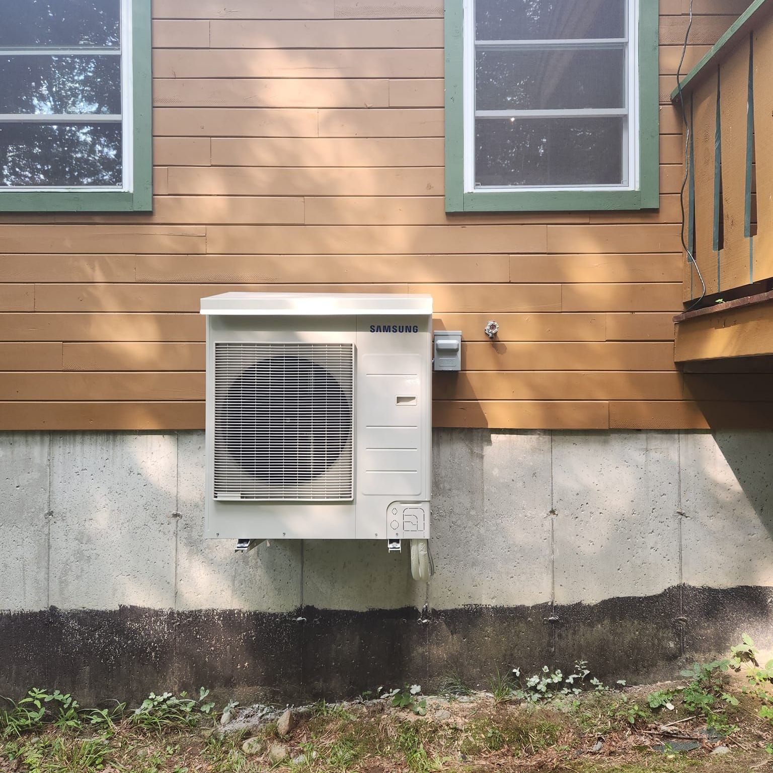 An air conditioner is sitting on the side of a brick building.