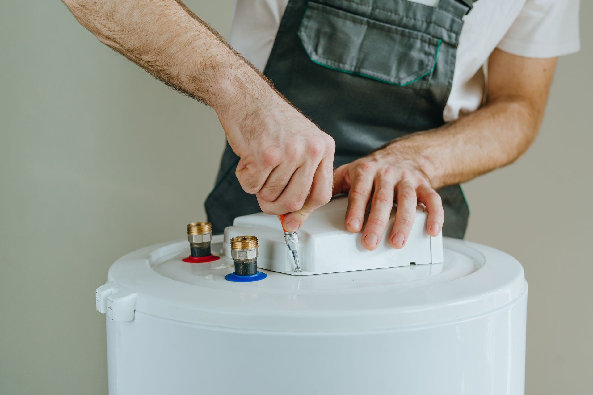 Hands tightening a valve on a white water heater with exposed fittings and pipes