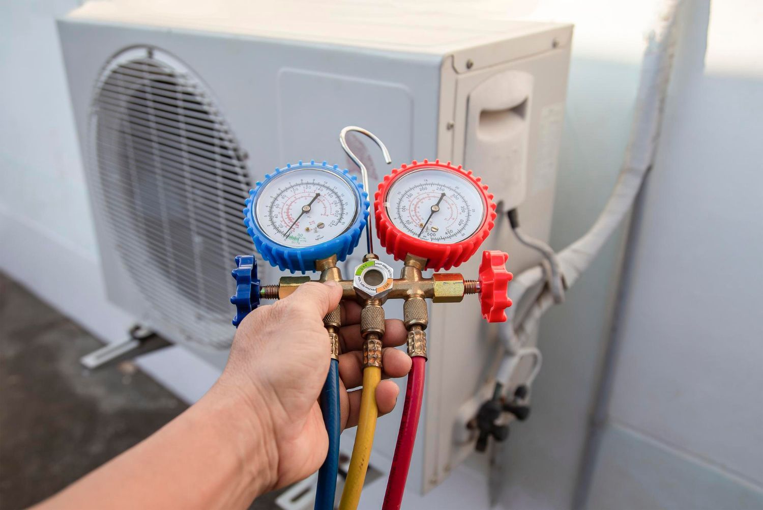 A person is holding a pair of gauges in front of an air conditioner.