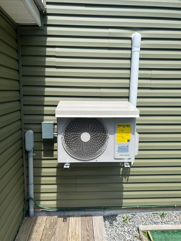 A gray air conditioner is sitting on the side of a brick building.