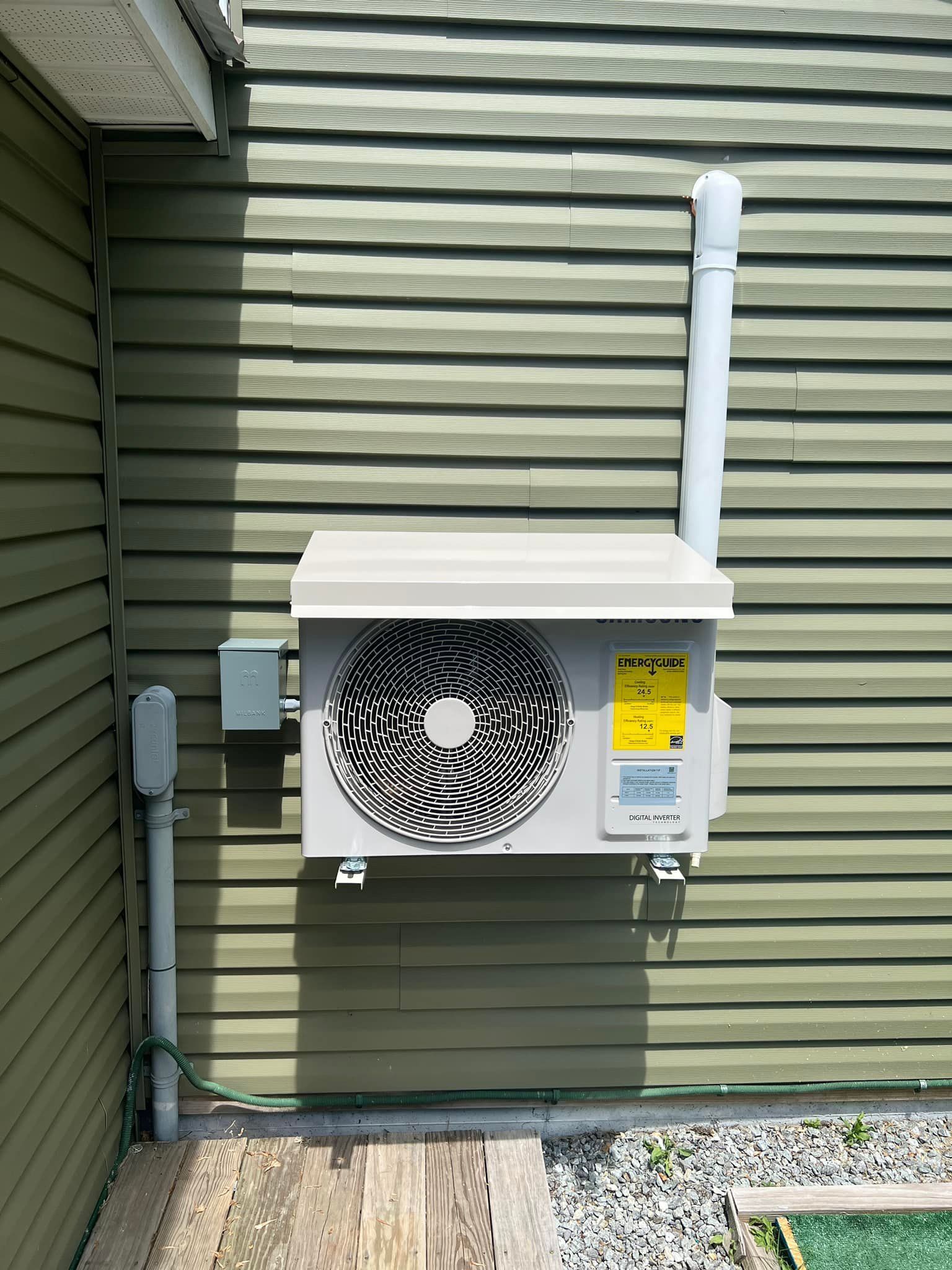 A white air conditioner is mounted on the side of a green house.