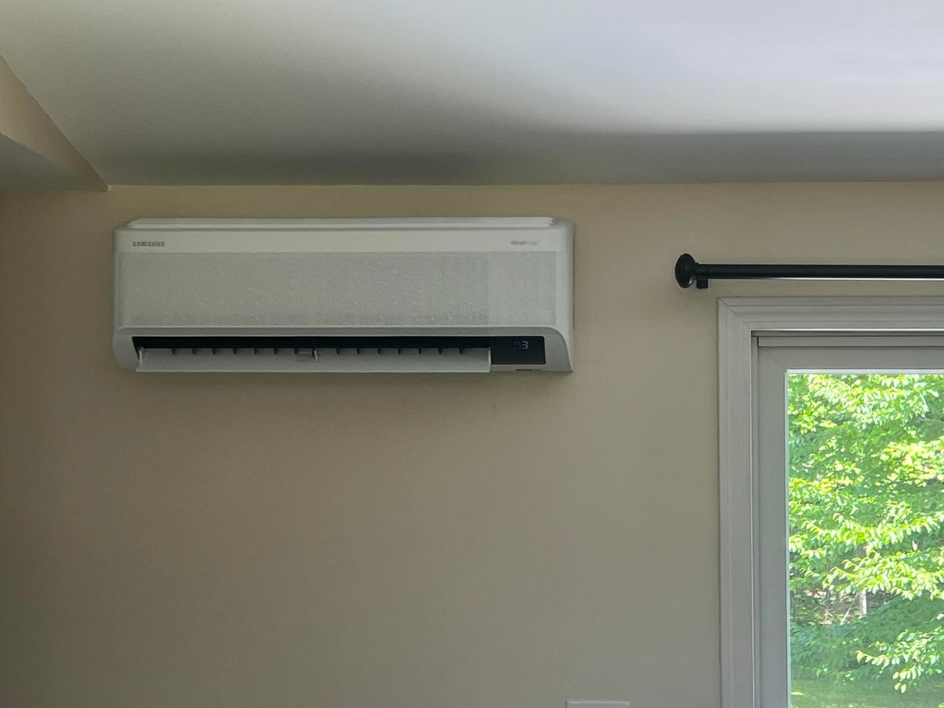 A white air conditioner is mounted on a wall next to a window.