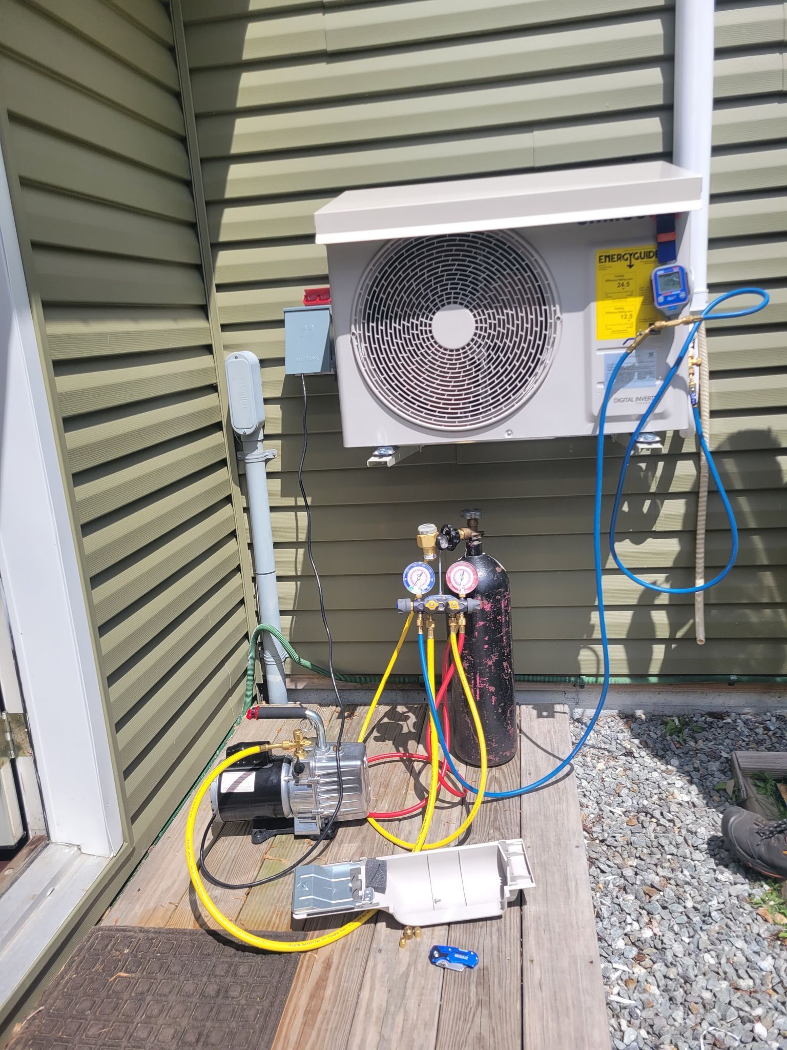 A man is standing on a ladder fixing an air conditioner on the side of a building.
