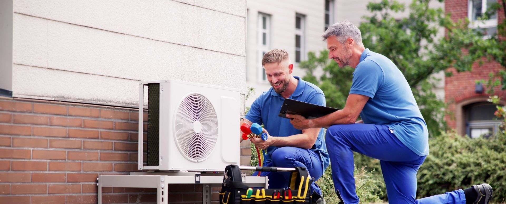 Two men are working on an air conditioner outside of a building.