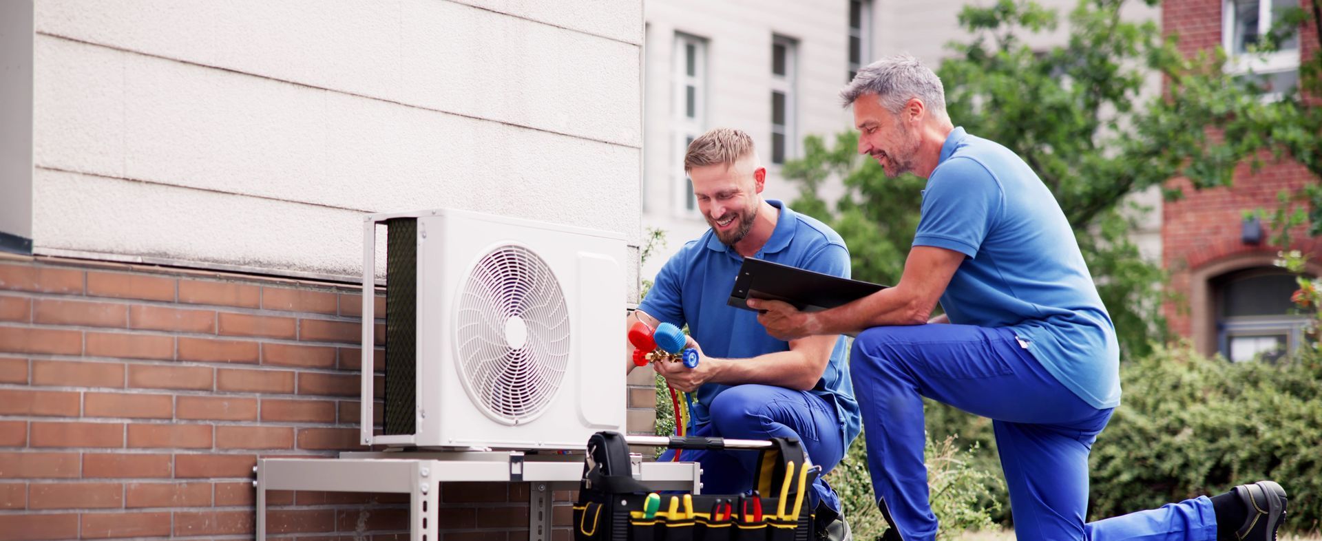 Two men are working on an air conditioner outside of a building.