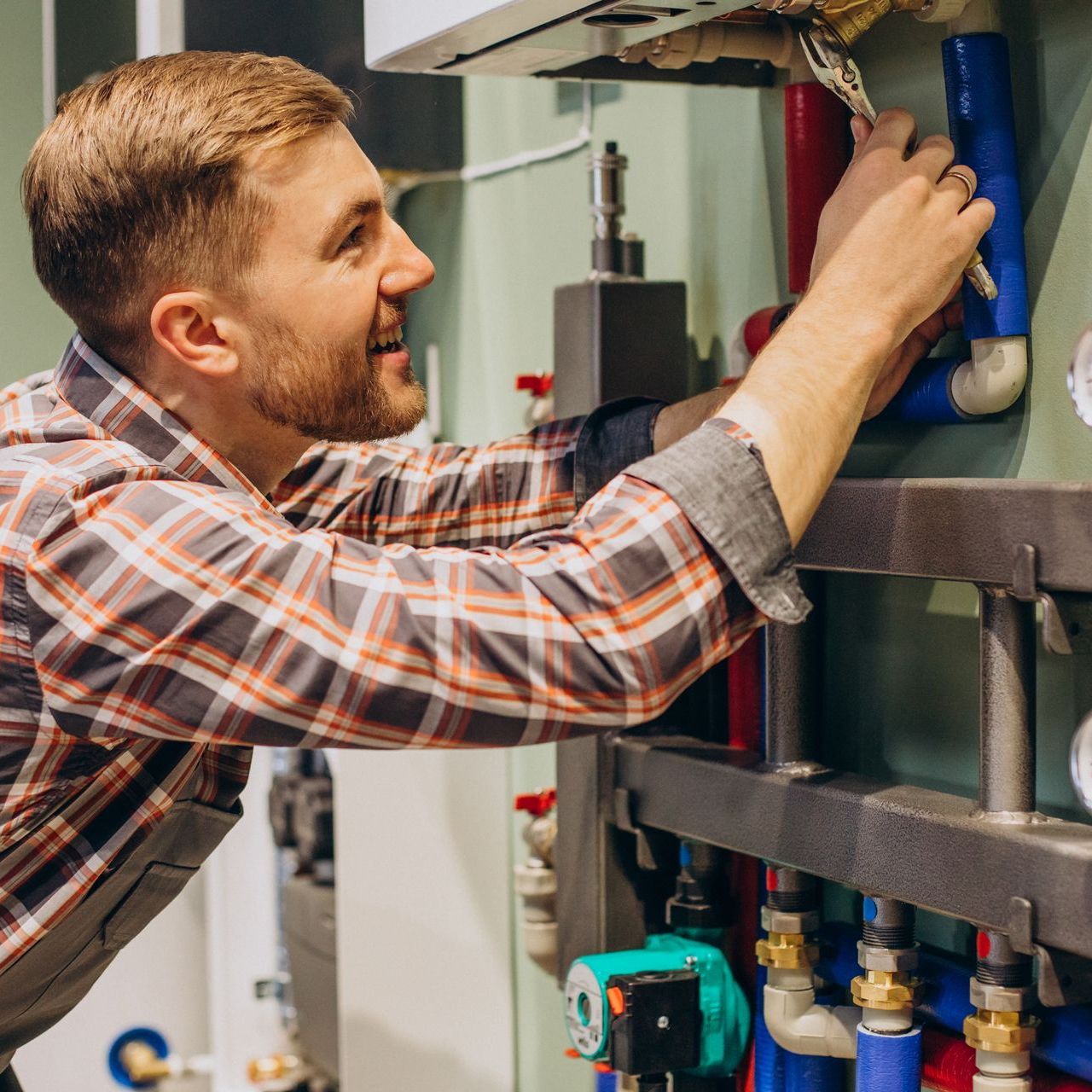 A man is working on a boiler with a wrench.