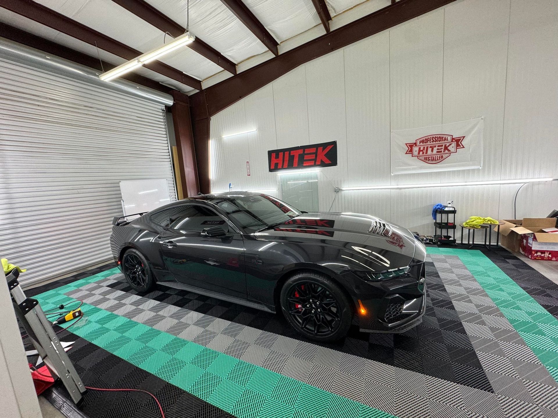 A black car is parked in a garage with a checkered floor.