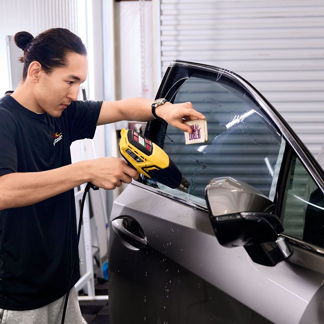 A person wearing blue gloves is applying ceramic coating to an application pad in front of a car.