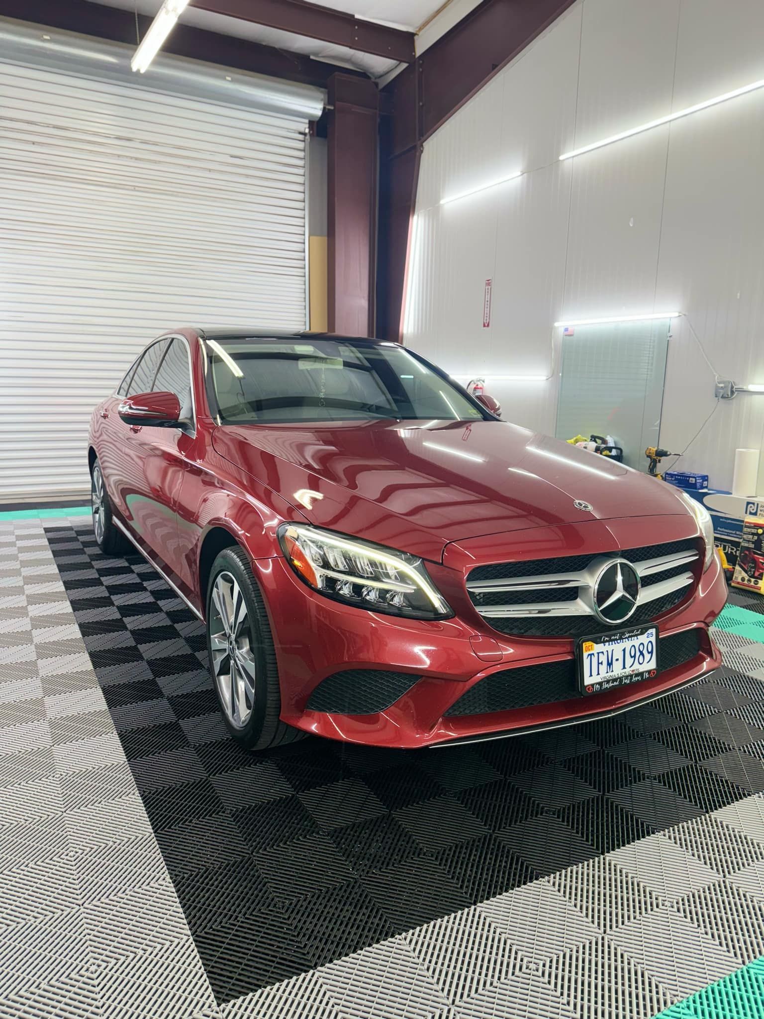 A shiny red Mercedes-Benz sedan parked inside a GT Tinting workshop, showcasing its sleek, tinted windows on a clean, patterned floor.