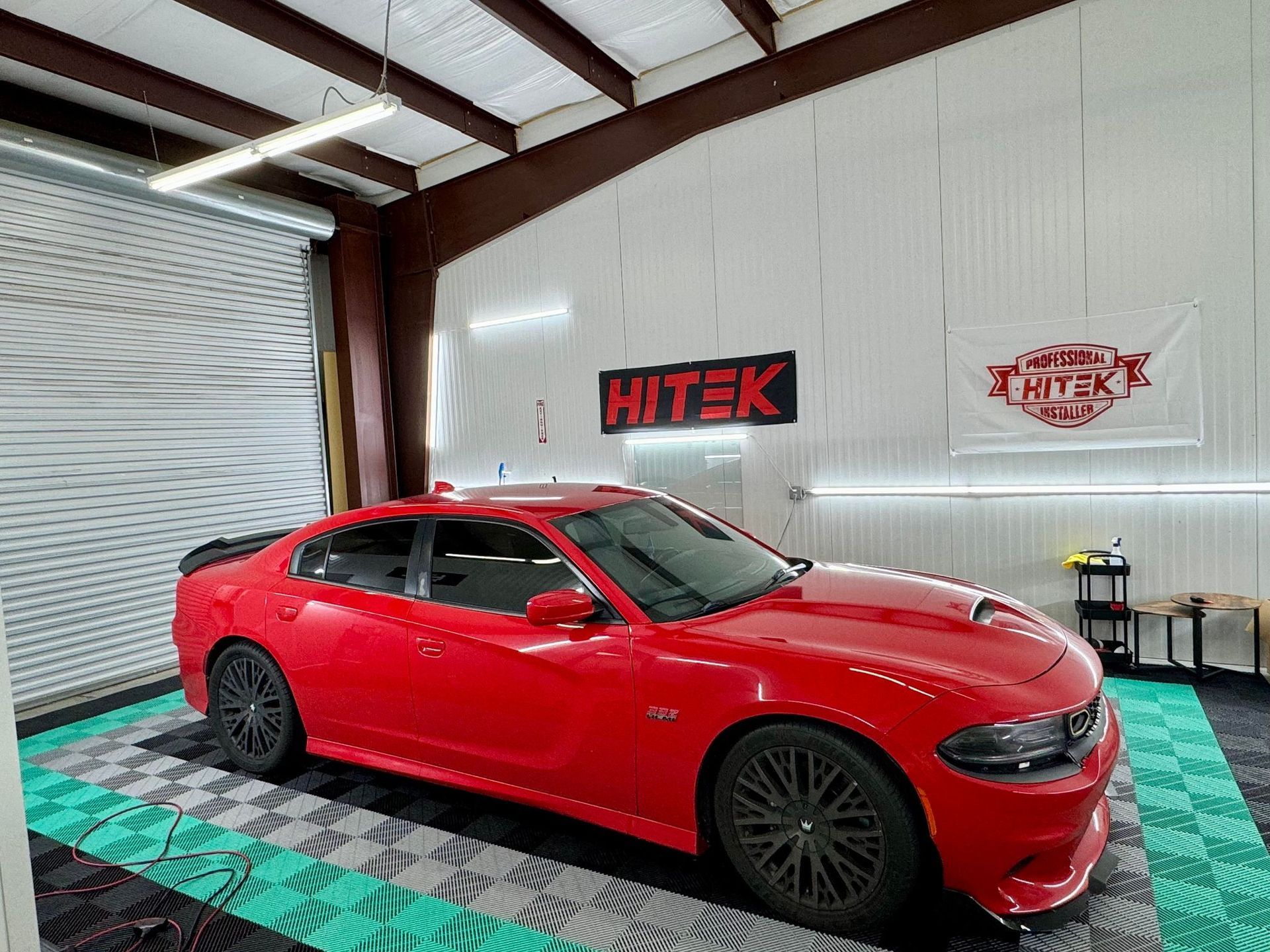 A black car is parked on a checkered floor in a garage.