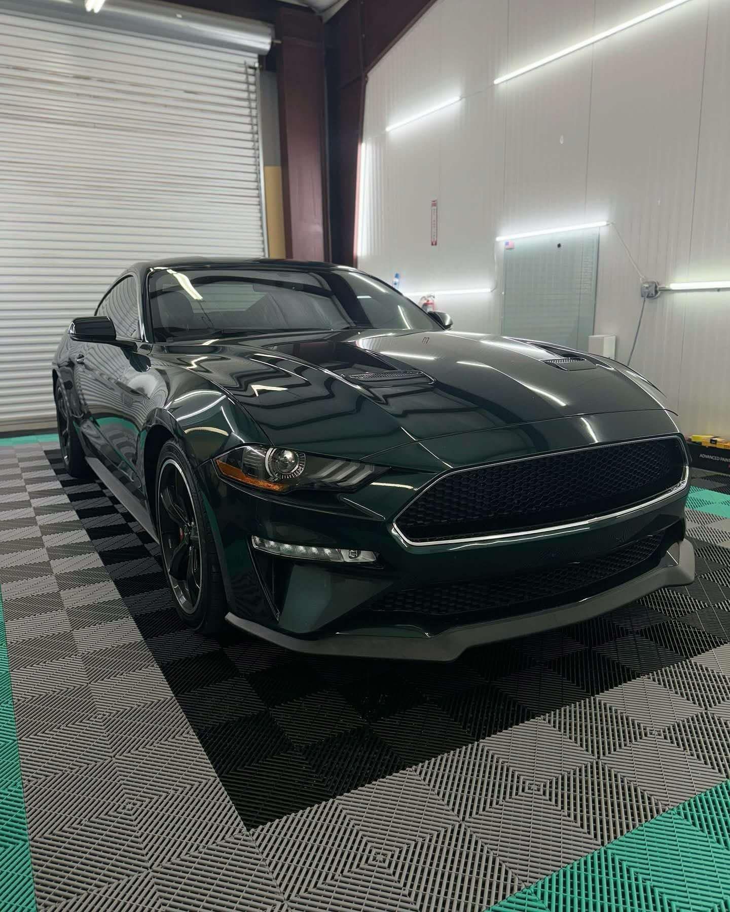 Shiny black Mustang with front windshield tint, parked inside a professional tint shop with modern lighting and flooring.