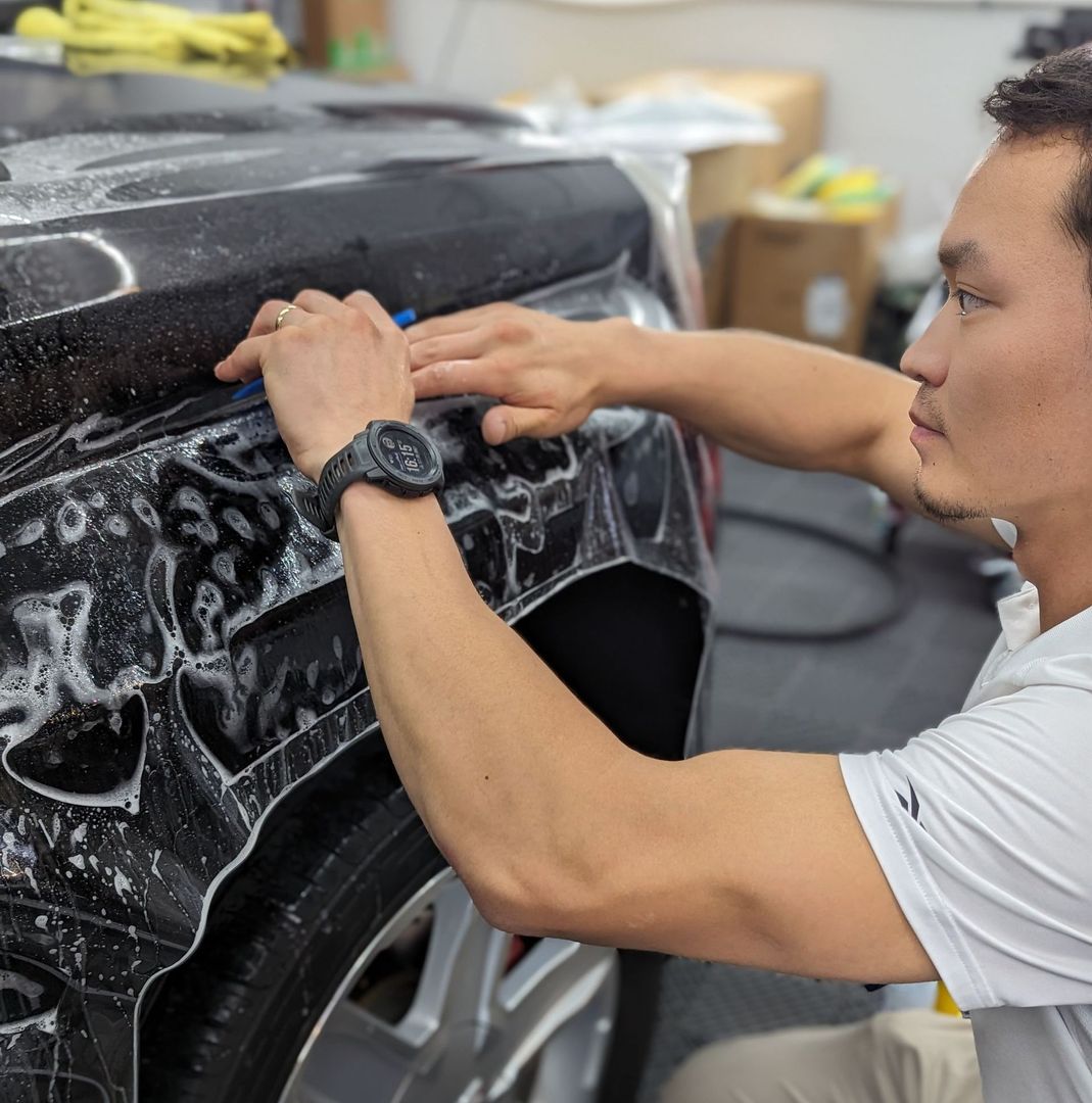 A man wearing a watch is cleaning the fender of a car.