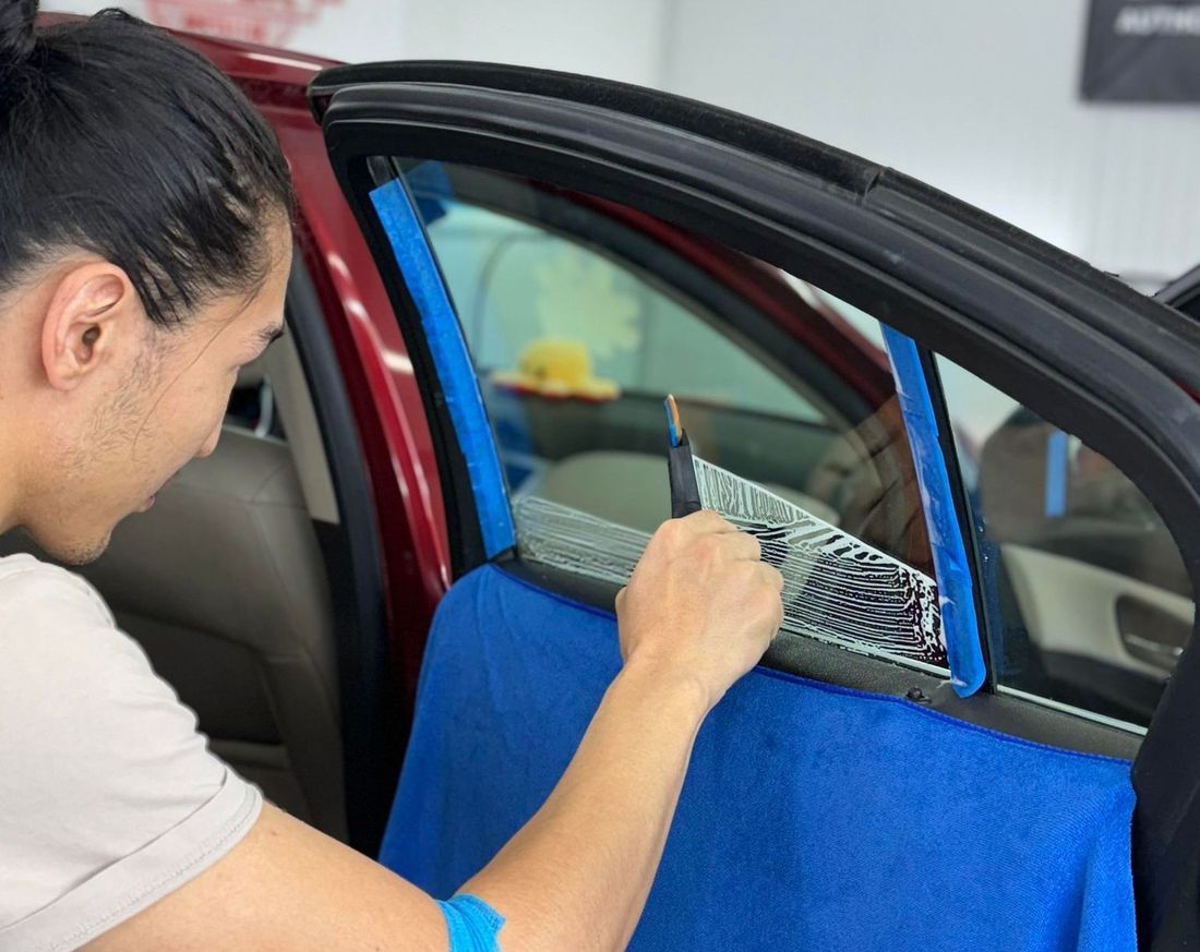 A man is applying window tinting to a car window.