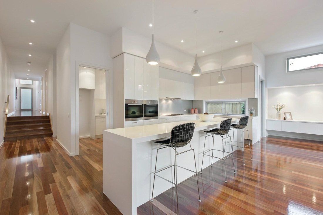 A kitchen with hardwood floors and white cabinets and stools.