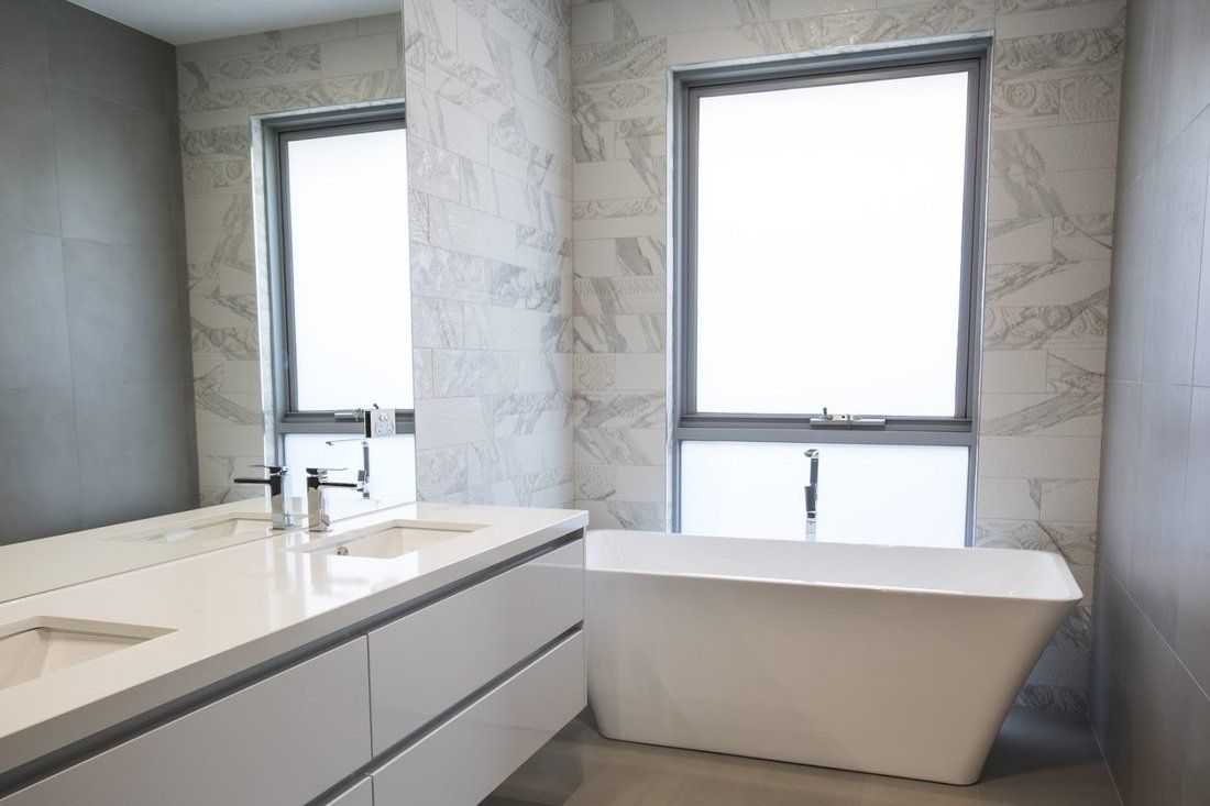 A bathroom with a tub , sink , mirror and two windows.