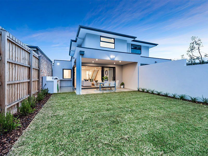 The backyard of a house with a large lawn and a wooden fence.