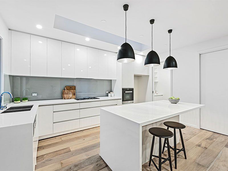 A kitchen with white cabinets , wooden floors , a large island and stools.