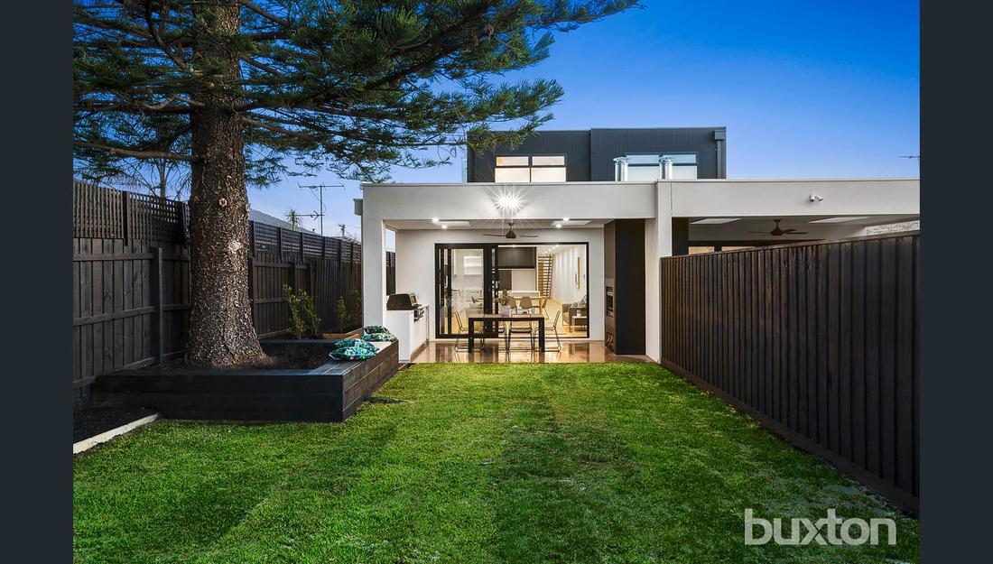 The backyard of a house with a large lawn and a fence.
